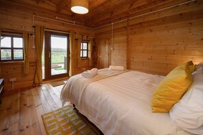 A wooden cabin bedroom with a bed, curtains, and a view through the door.