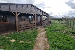 Ein hölzernes Gebäude mit einer Veranda und einem Feldweg, der davorhin führt.