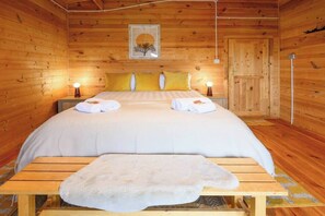 Ein Schlafzimmer in einer Holzhütte mit einem Bett, zwei Nachttischlampen, einem gerahmten Bild an der Wand und einer Holztür.