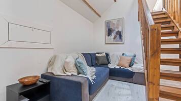 A modern living room with a blue sofa, a wooden bowl on a side table, and a wooden staircase.
