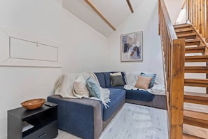 A modern living room with a blue sofa, a wooden bowl on a side table, and a wooden staircase.