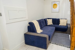 A modern living room with a blue sectional sofa, a small ottoman, and a patterned rug.