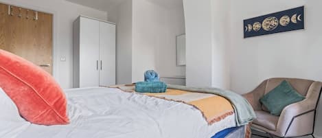 A bedroom with a bed, a chair, a wardrobe, and a wall art piece.