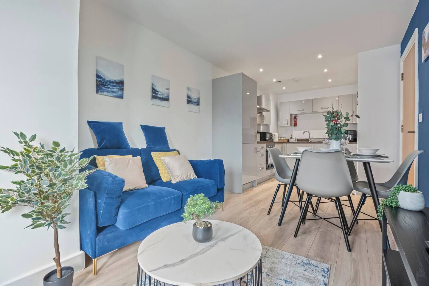 Un salon moderne avec un canapé bleu, une table à manger et des chaises, et une cuisine en arrière-plan.