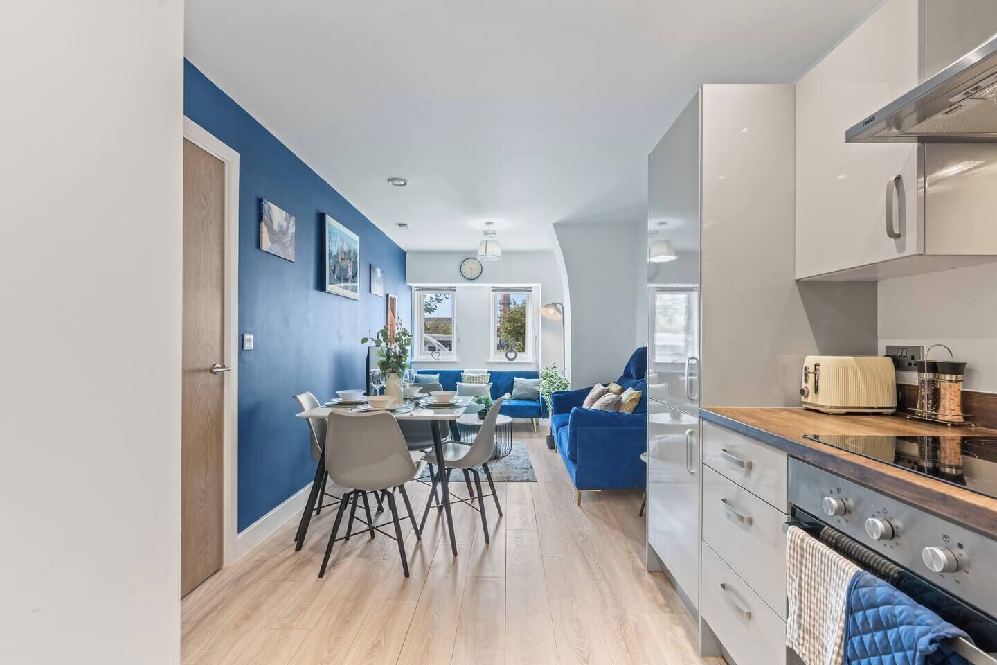 A modern kitchen with a built-in oven and a dining area with a blue sofa and a table set for two.