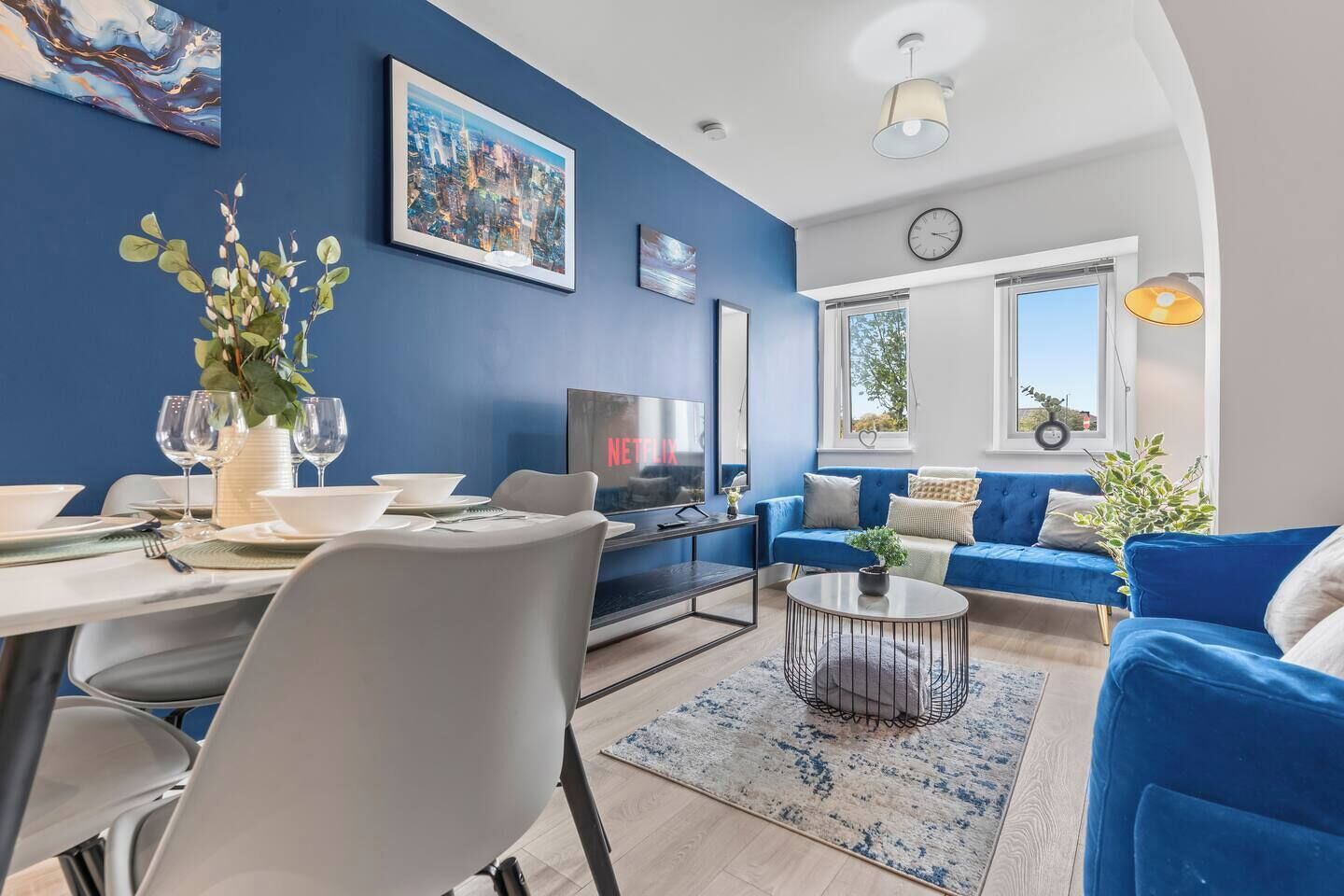 A modern living room with a blue sofa, a dining table set for four, and a television.