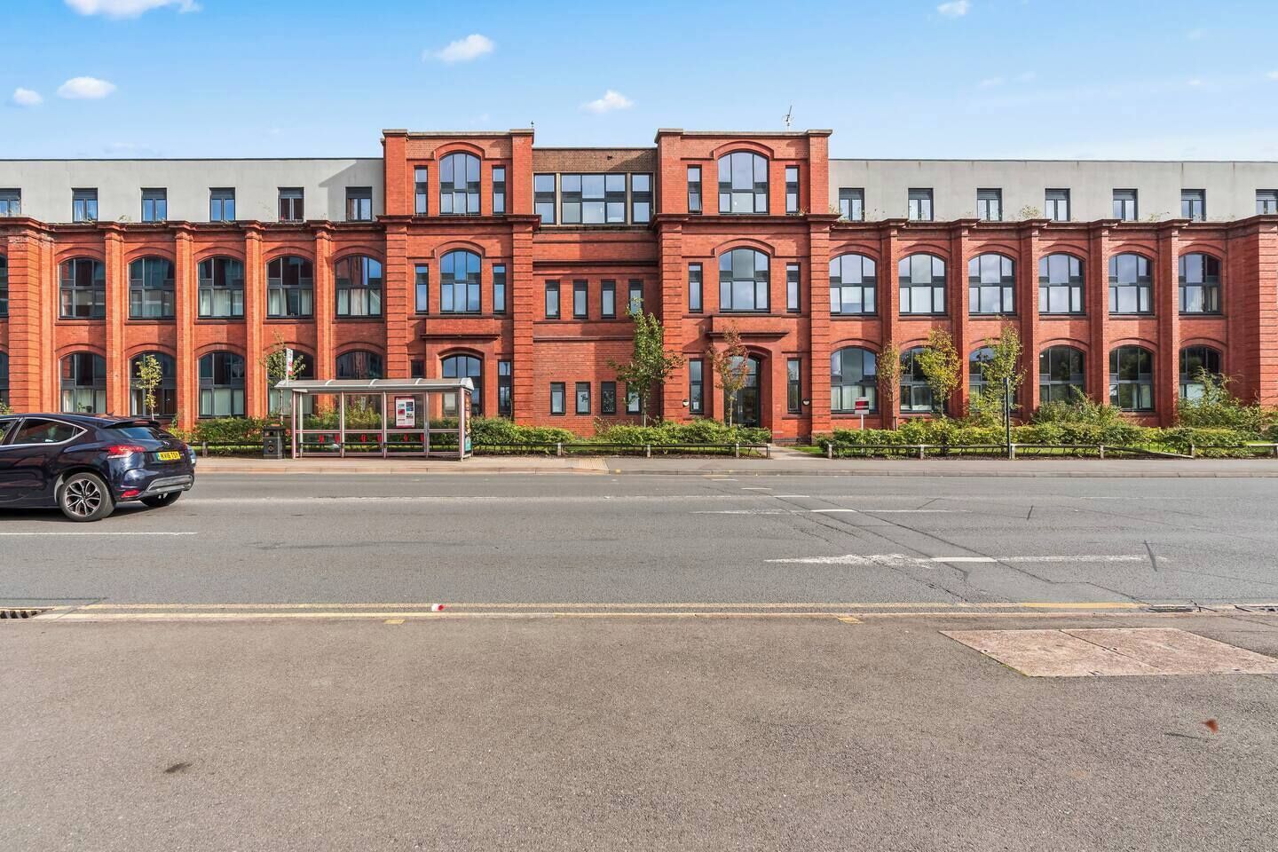 Een gebouw van rode bakstenen met veel ramen en een overdekte bushalte ervoor.