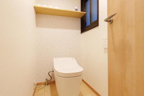 Une petite salle de bain avec des toilettes, une étagère au-dessus et une porte en bois.