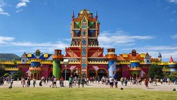 A colorful castle-like structure with multiple towers and a central spire, surrounded by a grassy area with people.