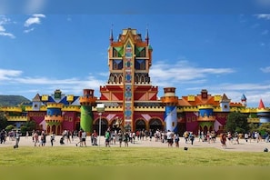 A colorful castle-like structure with multiple towers and a central spire, surrounded by a grassy area with people.