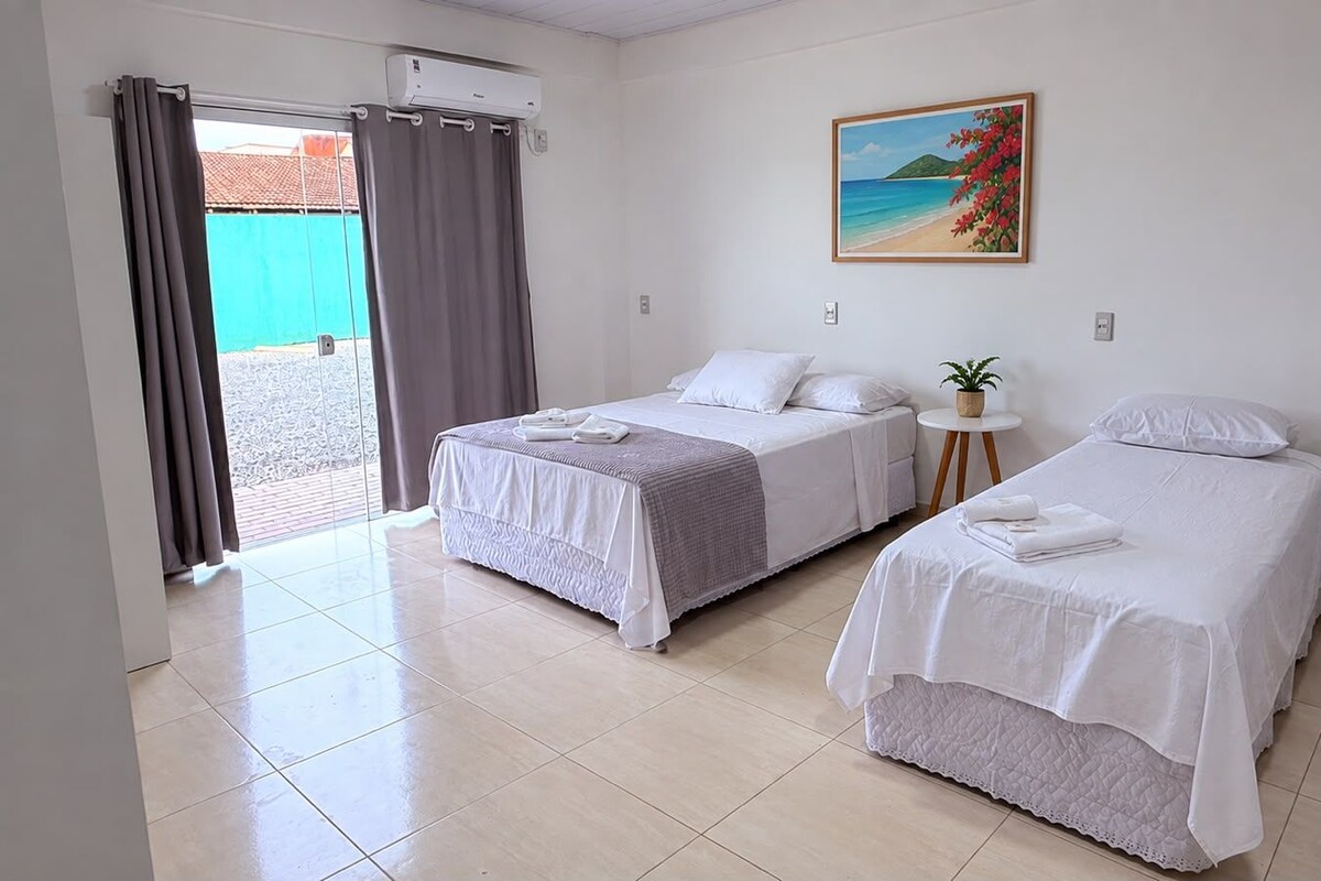 A hotel room with two beds, a painting, a small table with a plant, and a sliding door to an outdoor area.