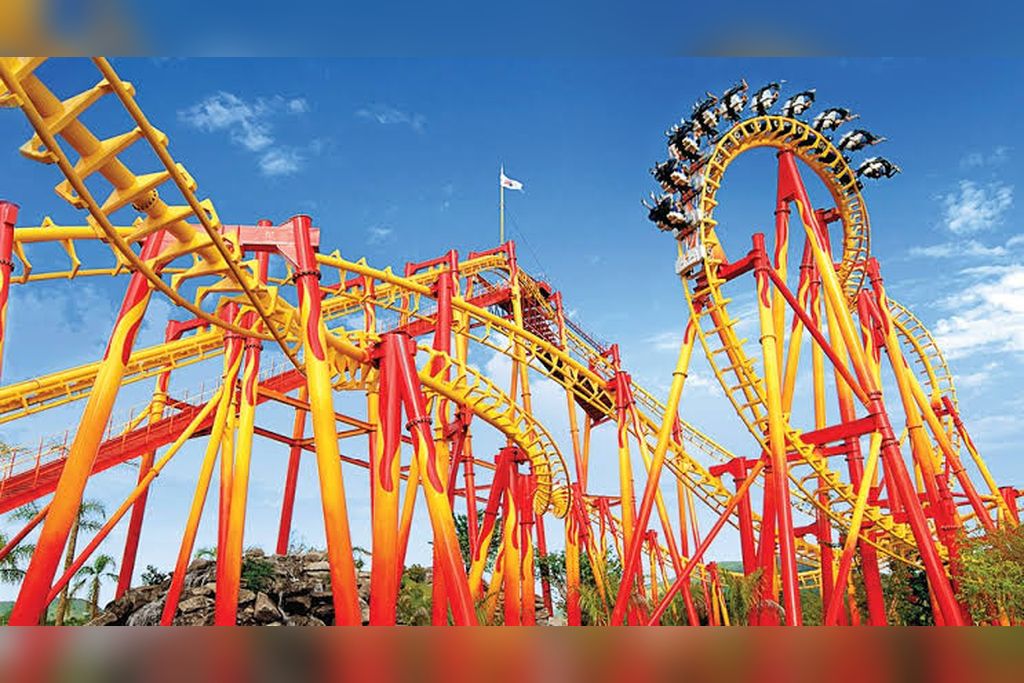 A roller coaster with a steep drop and a loop, set against a clear blue sky.