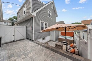 A two-story house with a patio area featuring a hot tub, outdoor seating, and a white fence.
