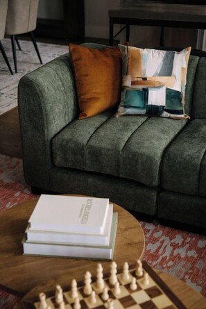 A green sofa with a cushion, a book, and a chessboard on a wooden table.