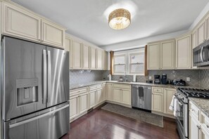 A modern kitchen with stainless steel appliances, light-colored cabinetry, and a patterned backsplash.