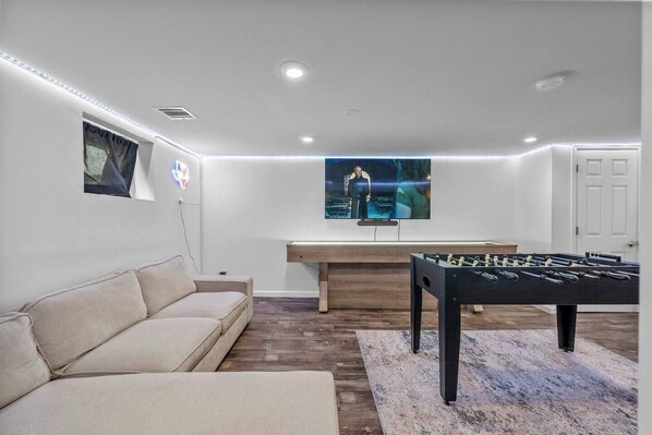 A modern living room with a sofa, a foosball table, and a flat-screen TV mounted on the wall. - Escape From Manhattan (North Bergen)