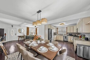 A modern kitchen with stainless steel appliances, a dining area with a wooden table set for four, and a living area with a sofa and a coffee table.