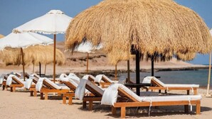 A beach with wooden lounge chairs and thatched umbrellas.