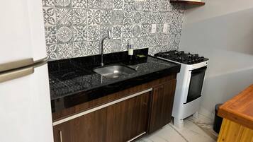 A kitchen with a black countertop, stainless steel sink, and a white stove.