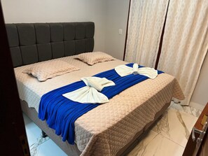 Uma cama com cabeceira acolchoada, edredom azul e duas toalhas dobradas em laços.