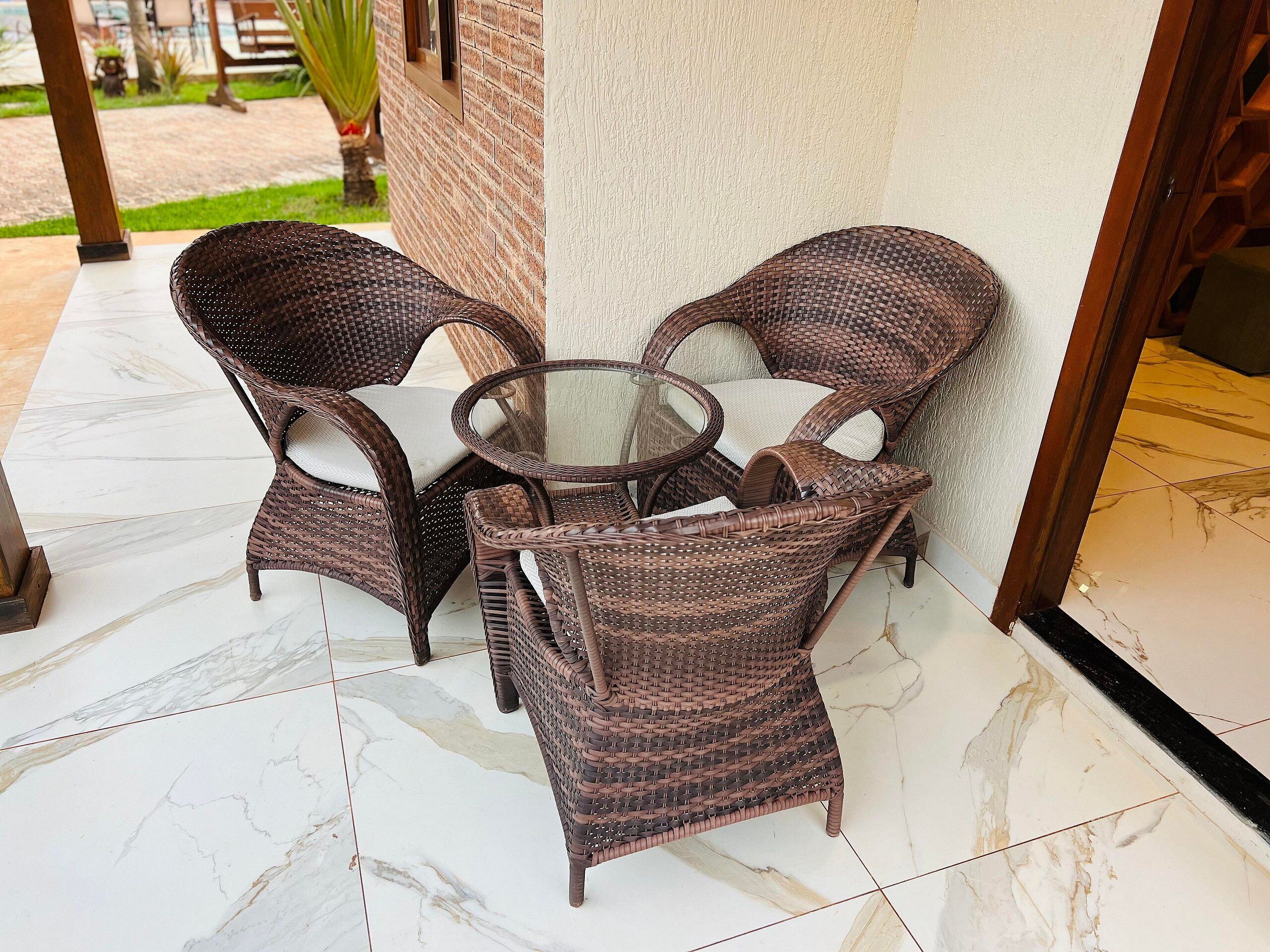 Um conjunto de cadeira de vime com mesa de vidro, posicionado sobre piso de azulejos próximo a uma entrada de edifício.
