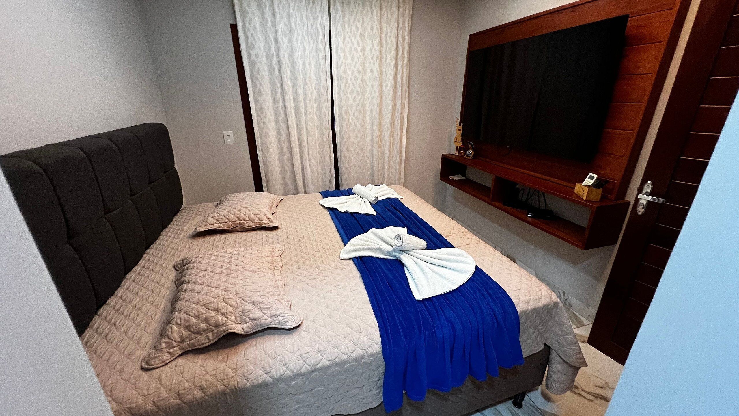 A hotel room with a bed, a television mounted on the wall, and a door.