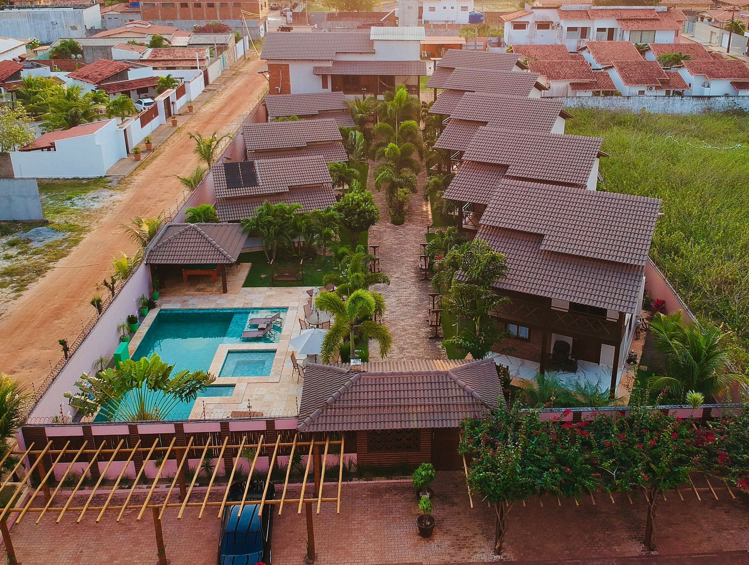 Un quartier résidentiel doté d’une piscine, de plusieurs maisons aux toits recouverts de tuiles rouges et d’un chemin piétonnier dallé.