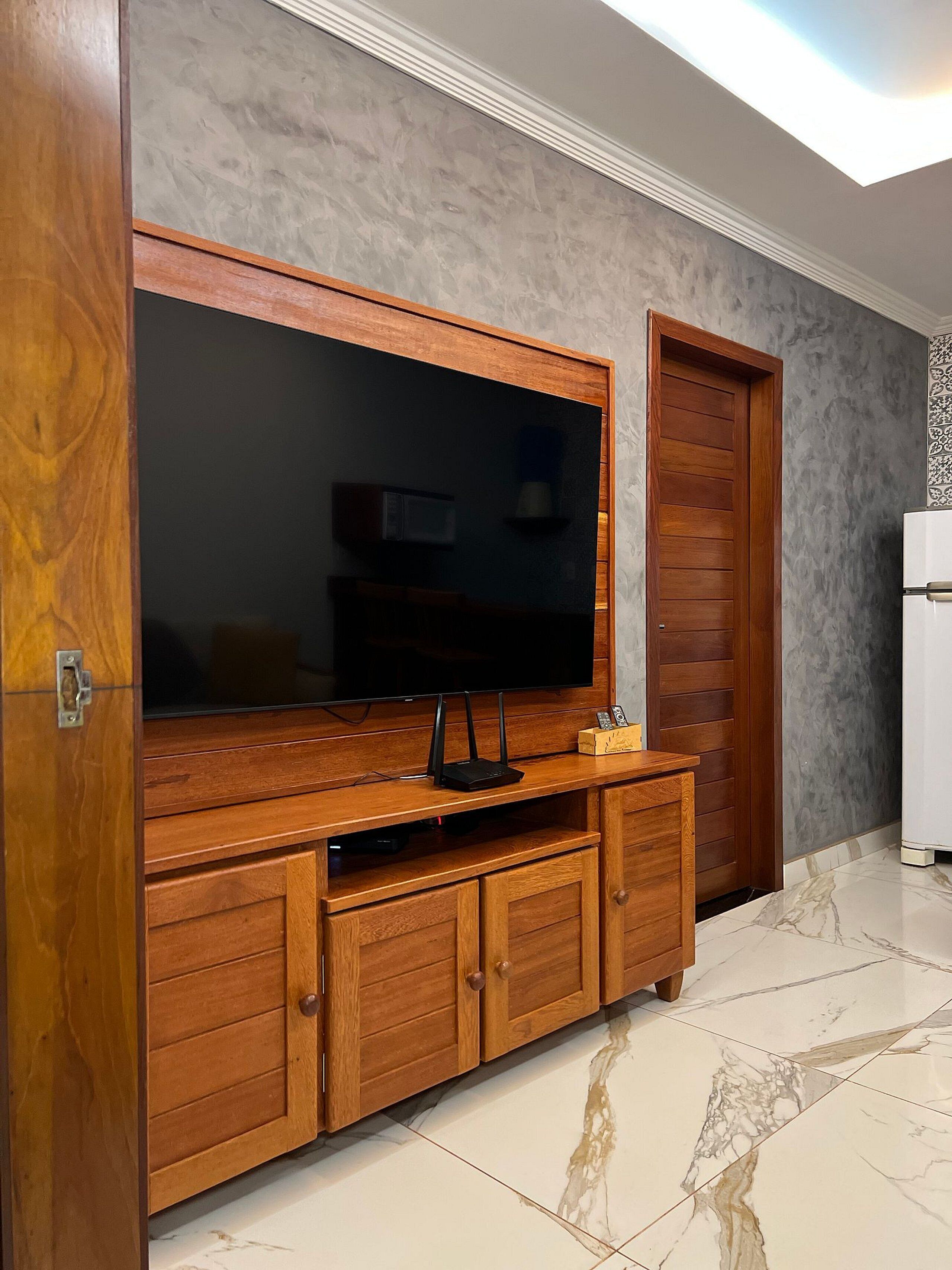 A wooden entertainment unit with a flat-screen TV, a soundbar, and a small cabinet.