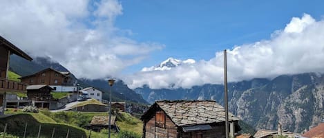 A mountainous village with traditional stone houses, a clear sky, and a snow-capped peak in the distance.