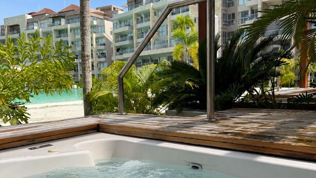 Una piscina con agua cristalina, rodeada de palmeras y con vistas a edificios de hotel al fondo.