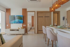 Ein modernes Wohnzimmer mit Flachbildfernseher, einer Couch, einem Essbereich mit Barhocker und einer Küche mit Spüle aus Edelstahl.
