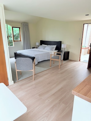 Een slaapkamer met een bed, nachtkastjes, een stoel en uitzicht op groen.