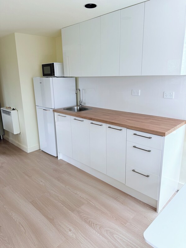 A kitchen with white cabinets, a wooden countertop, a built-in microwave, and a sink.