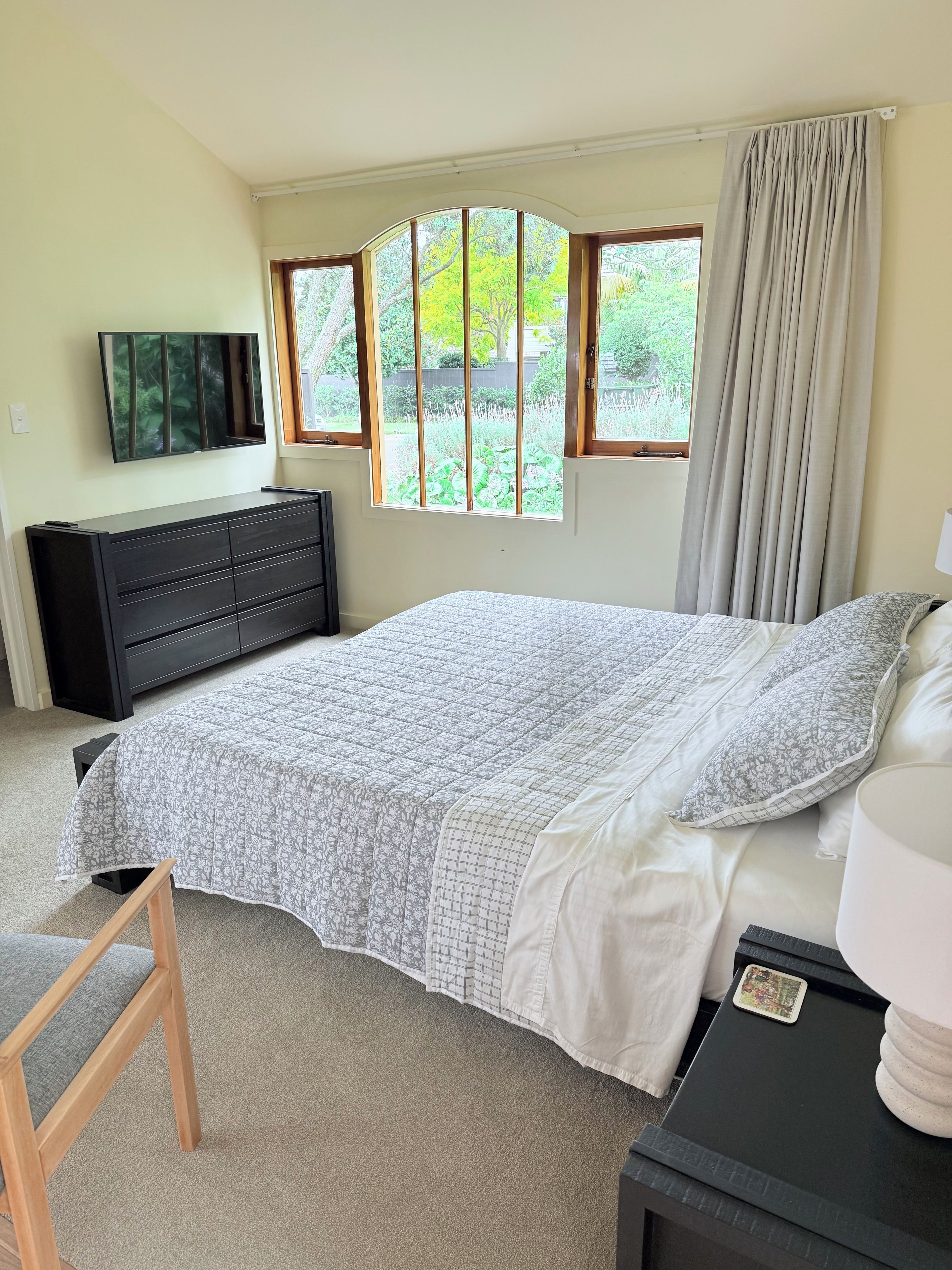 A bedroom with a bed, a dresser, a TV, and a window with curtains.