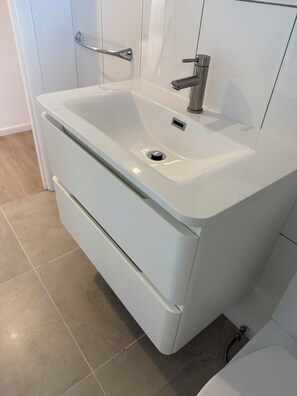 Une salle de bain moderne avec un lavabo blanc, un miroir et un porte-serviettes.