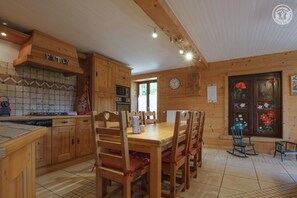 A wooden interior with a dining table, chairs, and a kitchen area including a microwave and oven. - The Bisanne Mill: The Beaufortain Balcony (VILLARD SUR DORON)