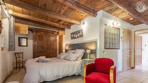 Ein Schlafzimmer mit einem Bett, einem Nachttisch, einem roten Sessel, Holzbalken an der Decke und einem Holzschrank.