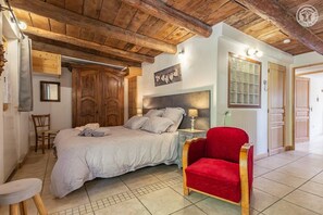 A bedroom with a bed, a nightstand, a red chair, wooden ceiling beams, and a wooden wardrobe. - The Bisanne Mill: The Beaufortain Balcony (VILLARD SUR DORON)