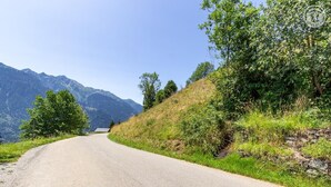 Eine kurvenreiche Bergstraße unter blauem Himmel, gesäumt von üppigem Grün.