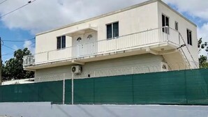 Een gebouw met twee verdiepingen en een balkon, omgeven door een groene hekken.