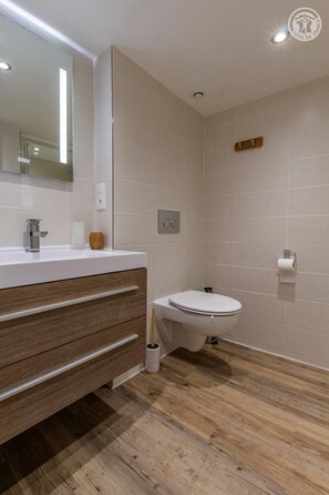 Ein modernes Badezimmer mit einem Holzlagerflächenschrank, einer Toilette und einem großen Spiegel.
