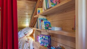 Ein Holzinnenraum mit schrägem Dach, einem Bett mit weißer Bettdecke und Regalen mit Büchern und Gesellschaftsspielen.