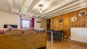 Ein Bett mit Holzkopf, ein Esstisch mit Stühlen, ein Heizkörper und Holzwände mit dekorativen Tellern.