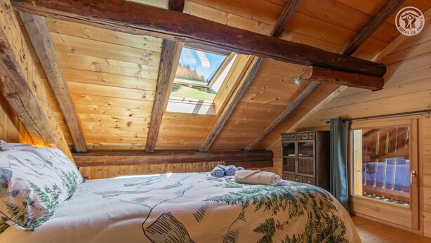 Ein Schlafzimmer einer Holzhütte mit einem Bett, einem Kleiderschrank und einem Fenster mit Vorhängen.