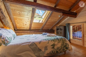 Quarto de cabana de madeira com cama, guarda-roupa e janela com cortinas.