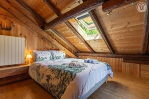 Ein gemütliches Schlafzimmer im Dachgeschoss mit Holzbalkendecke, einem Oberlicht, einem Bett mit alpiner Bettdecke und einer Nachttischlampe.