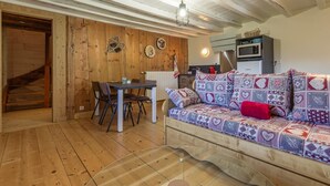 Ein gemütliches Zimmer mit Holzboden, einer Couch mit gemusterten Kissen, einem Esstisch mit Stühlen und einer Küchenzeile mit einer Mikrowelle.