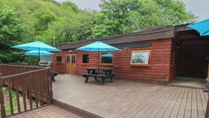 Une cabane en bois dotée d’une terrasse, de tables de pique-nique et de parasols bleus.