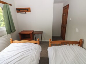 A small room with two wooden beds, a wooden table, a chair, a radiator, a window with a green curtain, and a wooden door. - CABIN NO. 4 - SALT AND FERN CABINS, family friendly in Port Talbot (Port Talbot)