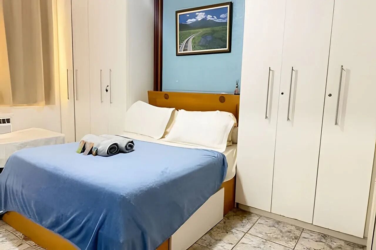 Un dormitorio con cama, ventana con cortinas, un cuadro en la pared y un armario.